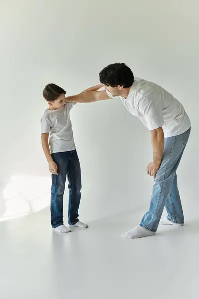 A father and son stand in a white room, the father leaning down towards the boy, suggesting a moment of playful interaction. — Stock Photo