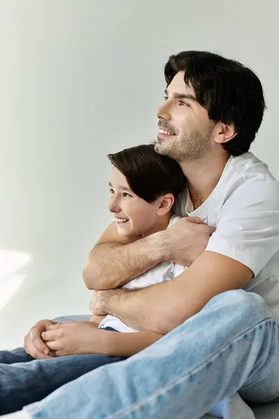 A father and son sit together, the fathers arm wrapped protectively around his son. They look up, sharing a moment of connection and warmth. — Stock Photo