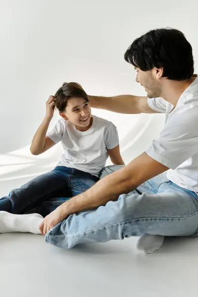 A father and son share a joyful moment, seated on the floor, the father gently ruffles his sons hair. — Stock Photo