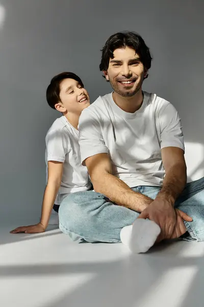 A father and son sit on a floor, bathed in sunlight, sharing a lighthearted moment. — Stock Photo
