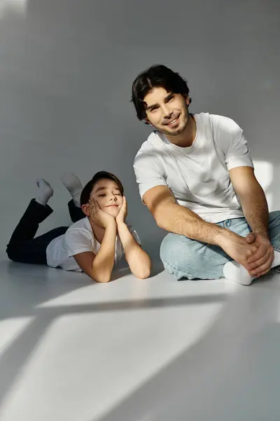 A father and son spend quality time together in a studio setting, with the father sitting and the son lying down. — Stock Photo