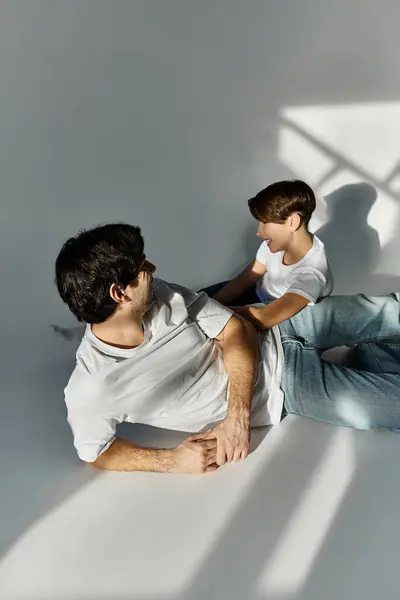 A father and son lay on a white floor, enjoying each others company. — Stock Photo