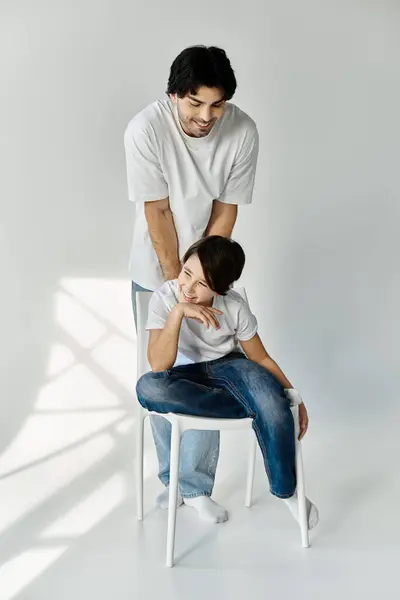 A father smiles down at his son who is sitting on a white chair. — Stock Photo