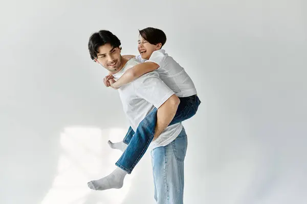 A father gives his son a piggyback ride in a white room. — Stock Photo