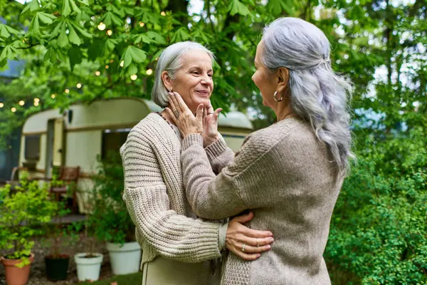 Two middle-aged women in cardigans embrace warmly outdoors. — Stock Photo