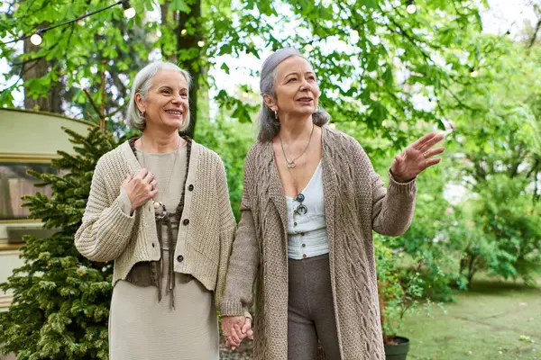 Two middle-aged women, a lesbian couple, are camping in a green forest near their van. They are smiling and walking together, enjoying the outdoors. — Stock Photo
