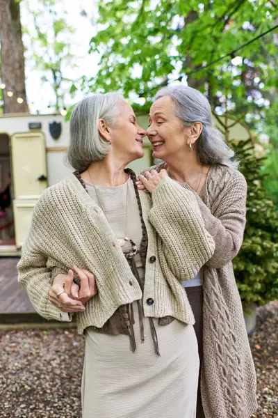 A middle-aged lesbian couple shares a tender moment while camping in a lush green forest, enjoying the beauty of nature together. — Stock Photo