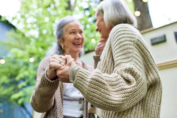 Two middle-aged women laugh and hold hands while camping in a green forest. They are in front of their camper van, enjoying a relaxing outdoor adventure. — Stock Photo