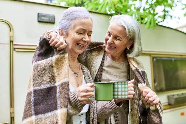 Two middle-aged lesbian women enjoy a cup of coffee while camping in the forest. — Stock Photo