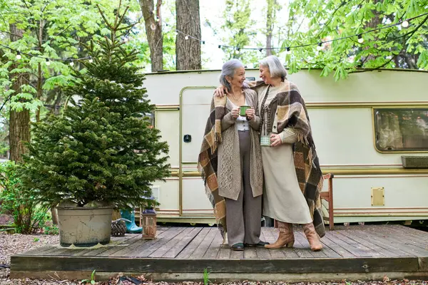 Um casal lésbico desfruta de uma bebida quente e um momento juntos enquanto acampam em uma floresta. — Fotografia de Stock