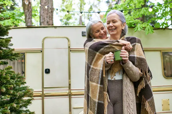 A lesbian couple, wrapped in a blanket, enjoys a cozy moment while camping in the forest. — Stock Photo