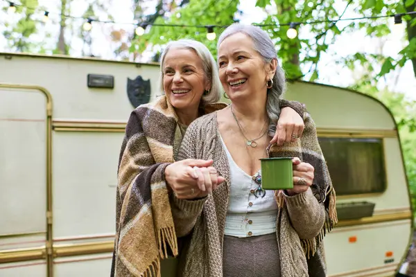 A lesbian couple smiles and embraces while camping in a green forest, enjoying the outdoors together. — Photo de stock