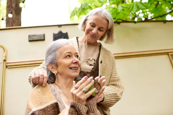 Two middle-aged women share a cup of coffee during a camping trip in a lush green forest. — Stock Photo