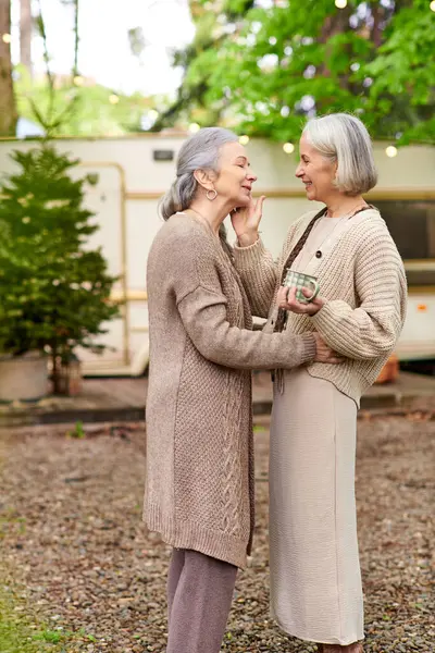 Two middle-aged women, a lesbian couple, stand close together in a forest setting near a camping van. — Photo de stock