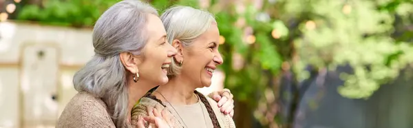 Two middle-aged women laugh together in a forest setting, near a camping van. — Stock Photo