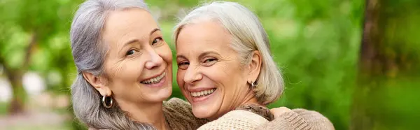 A close-up portrait of two middle-aged lesbian women smiling at the camera during their camping trip in a green forest. — Stock Photo