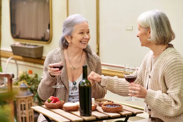 Two middle-aged women laugh and share a bottle of wine while camping in a forest near their van. — Stock Photo