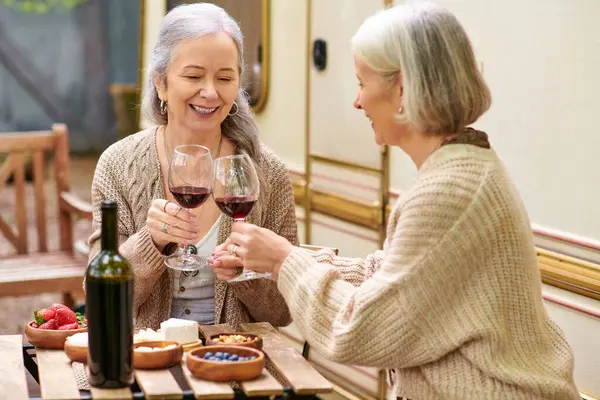 Two middle-aged women raise a toast with wine glasses while camping in a lush green forest. — Stock Photo