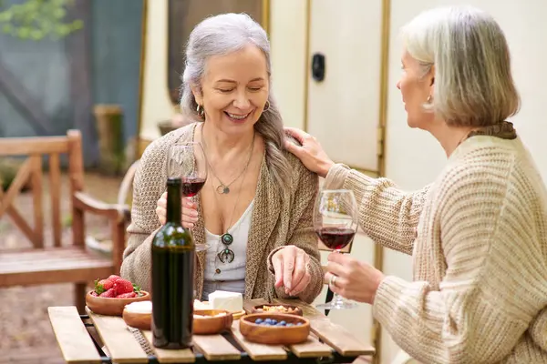 Dos mujeres disfrutan del vino y la risa mientras acampan en el bosque. - foto de stock