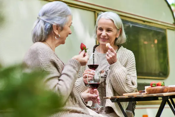 A middle-aged lesbian couple enjoys wine and snacks while camping in a lush green forest. — Stock Photo