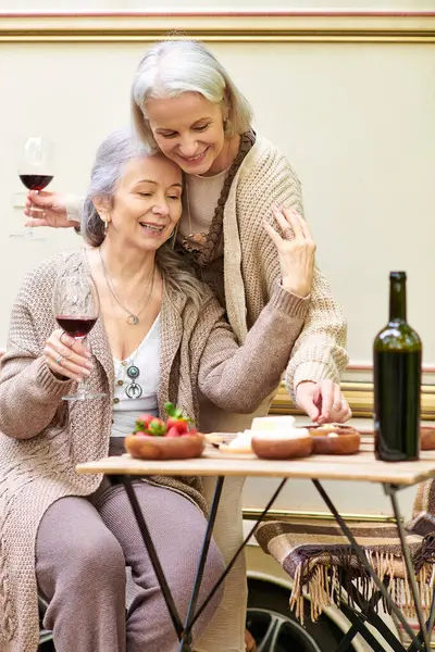 Zwei Frauen mittleren Alters lachen bei Wein und Snacks auf einem Campingplatz in der Nähe ihres Lieferwagens. — Stockfoto