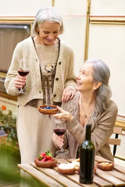 Two women enjoy a relaxing afternoon in the forest, sharing wine and laughter at a picnic table beside a camping van. — Stock Photo