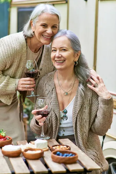 Two middle-aged women share a glass of wine while camping in a green forest, enjoying a romantic getaway. — Stock Photo
