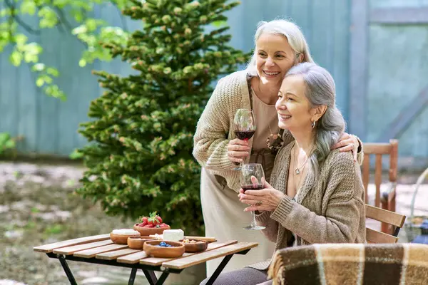 Two middle-aged women enjoying a glass of wine while camping in the forest. — Stock Photo