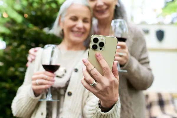 Two middle-aged women enjoy a glass of wine while camping in a green forest. — Stock Photo