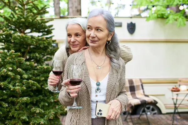 Um casal lésbico de meia-idade gosta de vinho e risos enquanto acampa em uma floresta exuberante. — Fotografia de Stock