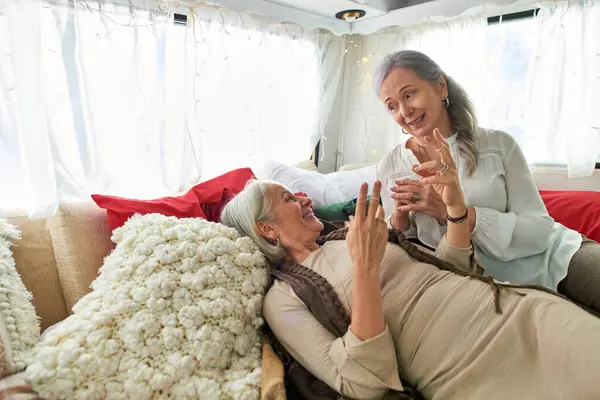 A lesbian couple, both middle-aged with gray hair, share a lighthearted moment while relaxing in a camping van. — Stock Photo