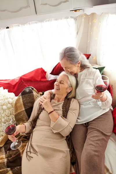 Two women, possibly a lesbian couple, cuddle and share wine inside a camping van. — Stock Photo
