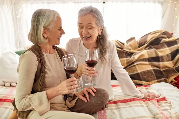 Two middle-aged women, a lesbian couple, enjoy a glass of wine while laughing together inside their camper van. — Stock Photo