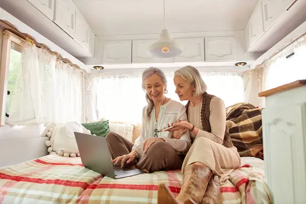 Two middle-aged women relax in a camper van, one using a laptop while the other looks on. — Stock Photo