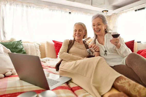 A lesbian couple enjoys a glass of wine and a laptop in their cozy camper van during their trip. — Stock Photo