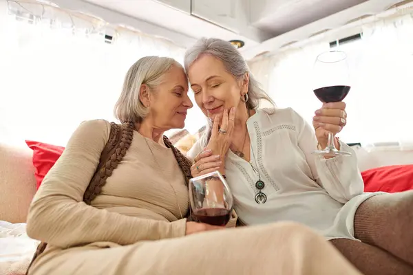 A lesbian couple shares a tender moment while enjoying wine inside their camper van during a road trip. — Stock Photo