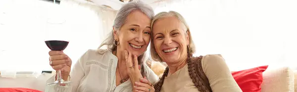 Dos mujeres de mediana edad están sonriendo y sosteniendo una copa de vino en una furgoneta de camping. - foto de stock