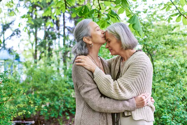 Um casal de lésbicas em cardigans abraçam-se ternamente sob a sombra de uma árvore frondosa, seu amor palpável em seu abraço. — Fotografia de Stock
