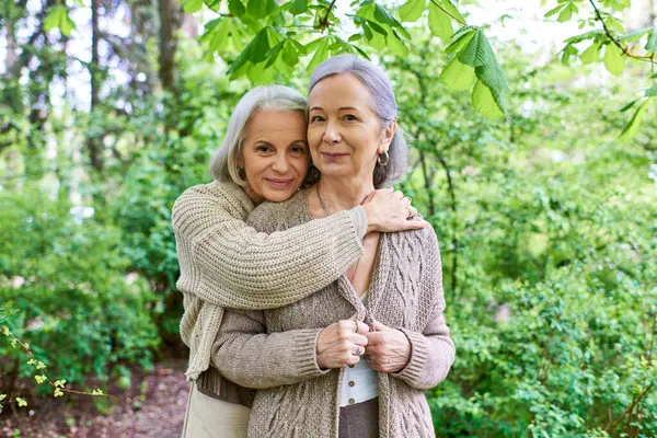 A lesbian couple in cardigans embraces in a lush forest setting. — Stock Photo