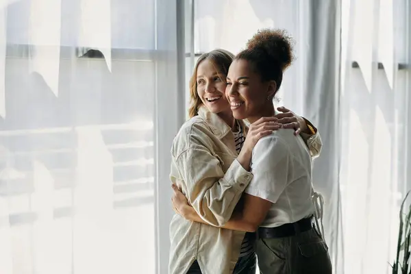Two women in casual wear, embracing near a window. — Stock Photo