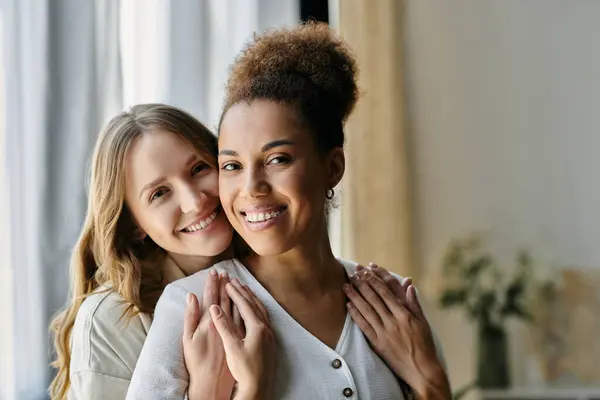 A diverse lesbian couple shares a tender moment at home, their smiles radiant with love and happiness. — Stock Photo