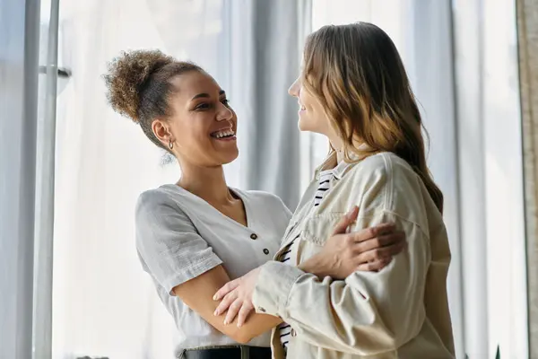 Zwei Frauen, eine mit blonden und eine mit lockigen braunen Haaren, umarmen sich in einem sonnigen Raum. — Stockfoto