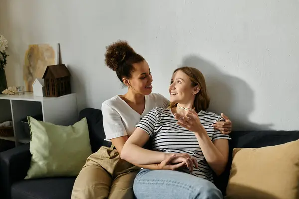 Due donne in abbigliamento casual coccole su un divano, ridendo e parlando. — Foto stock