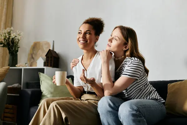 A lesbian couple relaxes on a couch at home, enjoying a cup of coffee and a conversation. — Stock Photo