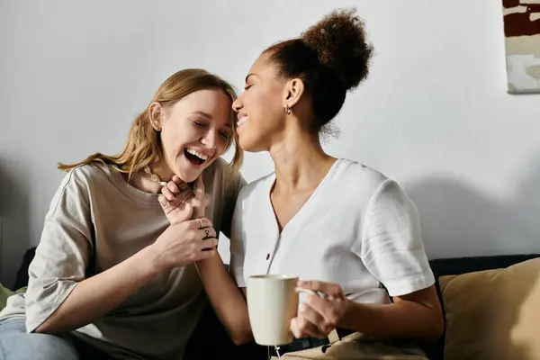 Різноманітна лесбіянка пара сміється разом, насолоджуючись затишним моментом вдома. — стокове фото