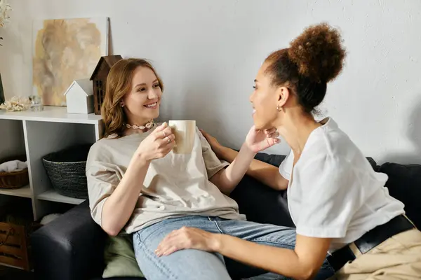 A diverse lesbian couple relaxes at home, enjoying a cup of coffee and each others company. — Stock Photo