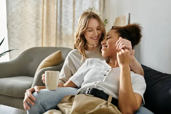 A diverse lesbian couple shares a loving moment on a couch, surrounded by the comfort of home. — Stock Photo