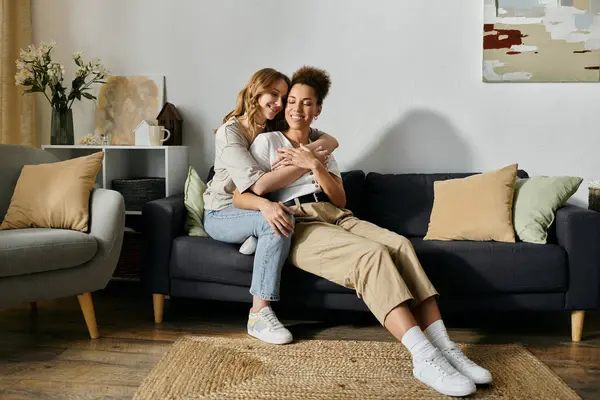 Una coppia lesbica si abbraccia su un divano in un soggiorno, mostrando il loro amore e connessione. — Foto stock