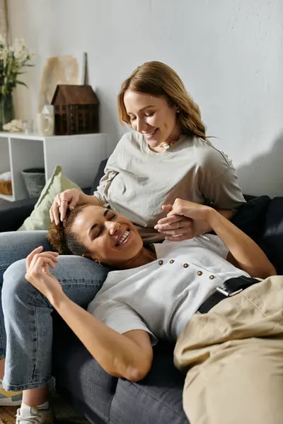 A lesbian couple, relaxed and happy, cuddles on a couch. — Stock Photo