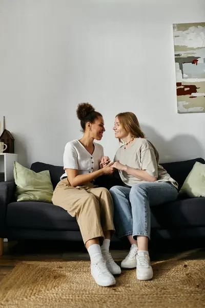 A diverse lesbian couple shares a moment of intimacy on a comfortable couch in their home. — Stock Photo